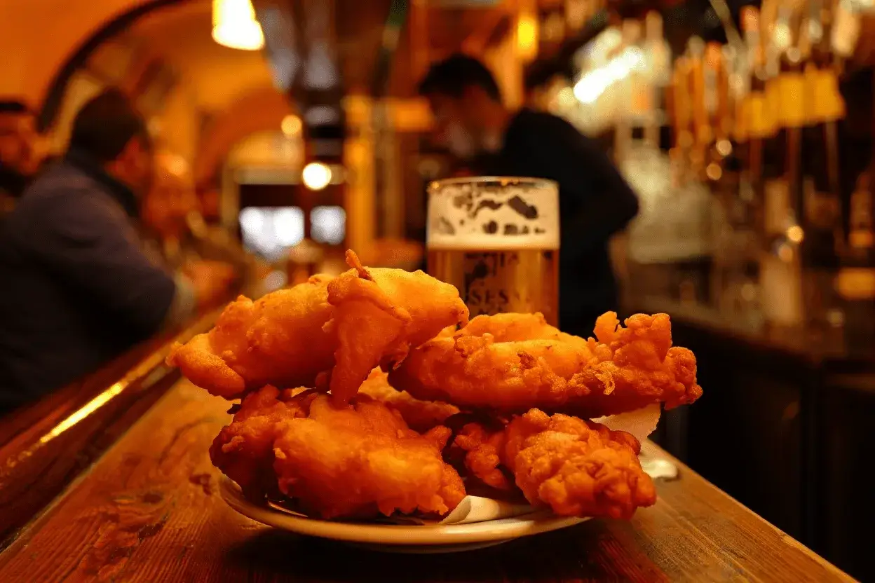 Un plato de pavía pescado, crujiente y dorado, junto a una cerveza espumosa en una barra de bar.