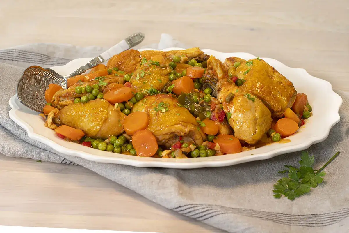 Sabroso estofado de pollo con zanahorias y guisantes, servido en una fuente blanca con una cuchara de plata.