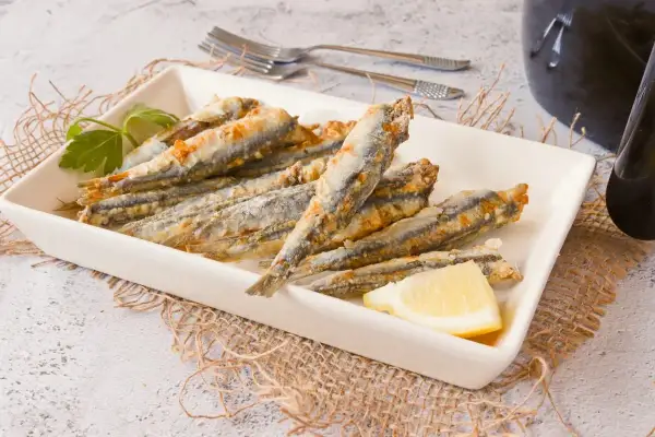 Boquerones en freidora de aire, dorados y crujientes, servidos en plato blanco con limón y perejil.