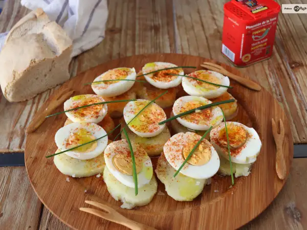 Deliciosos huevos a la gallega, cortados por la mitad y espolvoreados con pimentón, sobre rodajas de patata.