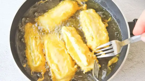 Soldaditos de pavia dorándose en aceite caliente. Un tenedor los voltea para una fritura perfecta.