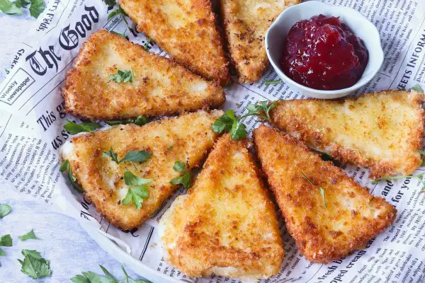 Triángulos de queso frito crujientes, servidos con un tazón de mermelada de frutos rojos.