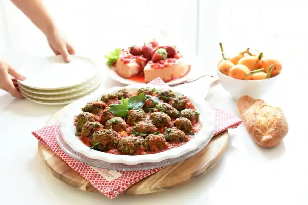 Albondigas de berenjenas en salsa roja, decoradas con albahaca, junto a un postre de fresas y pan.