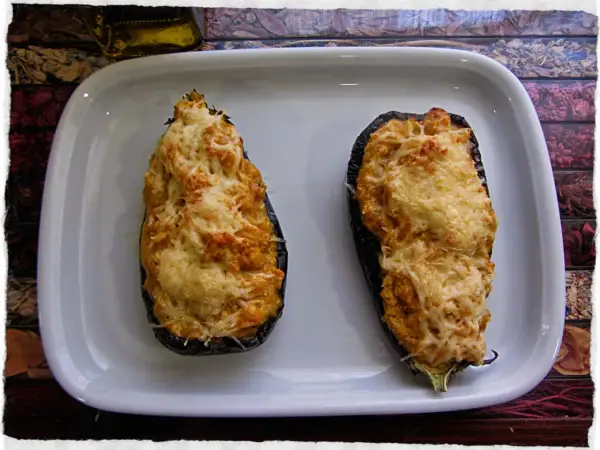 Dos berenjenas rellenas de gambas, gratinadas con queso, listas para disfrutar.