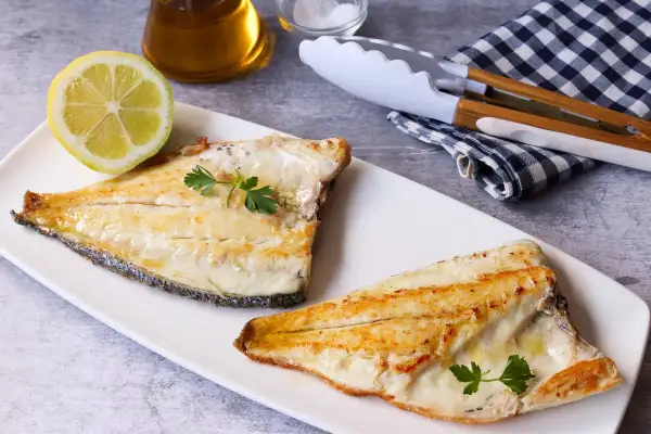 Dos filetes de dorada a la plancha, jugosos y dorados, servidos con perejil fresco y una rodaja de limón.