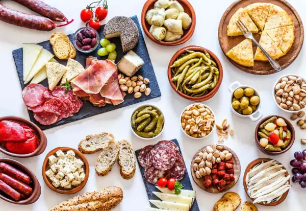 Gran variedad de aperitivos baratos para mucha gente: embutidos, quesos, aceitunas, frutos secos, pimientos, boquerones y tortilla.
