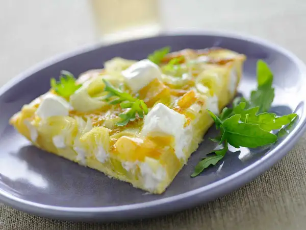 Porción de tortilla con puerros y queso de cabra, decorada con rúcula. Ideal para tus recetas con puerros.