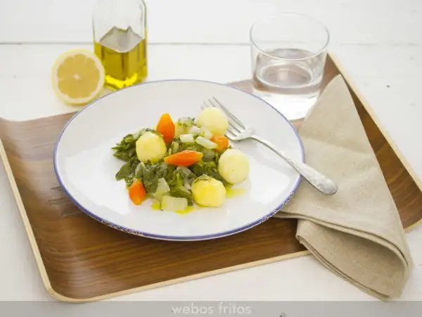 Plato de acelgas con patatas, zanahoria y cebolla, acompañado de limón, aceite de oliva y agua.