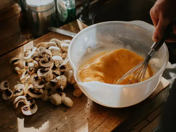 Un bol con huevos batidos y champiñones cortados en una tabla de madera, listos para un delicioso revuelto de setas.
