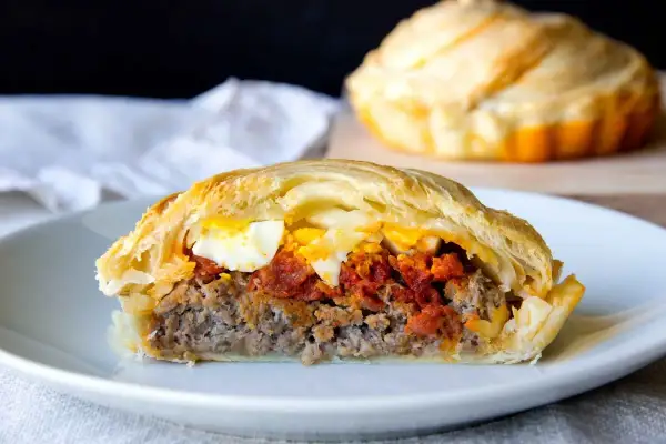 Porción de pastel de carne jugoso con huevo duro y salsa de tomate, envuelto en masa dorada.