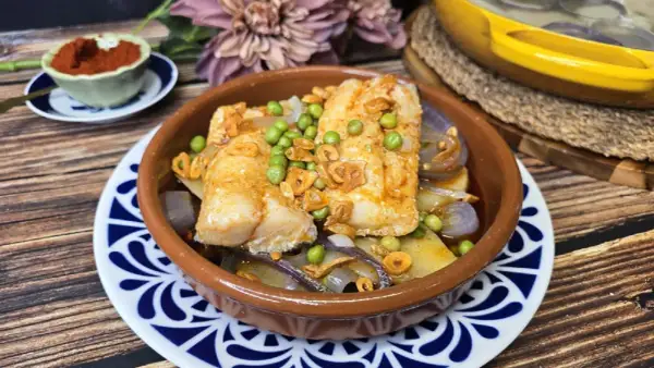 Bacalao a la gallega con patatas, guisantes y ajo frito en cazuela de barro. Un plato tradicional lleno de sabor.