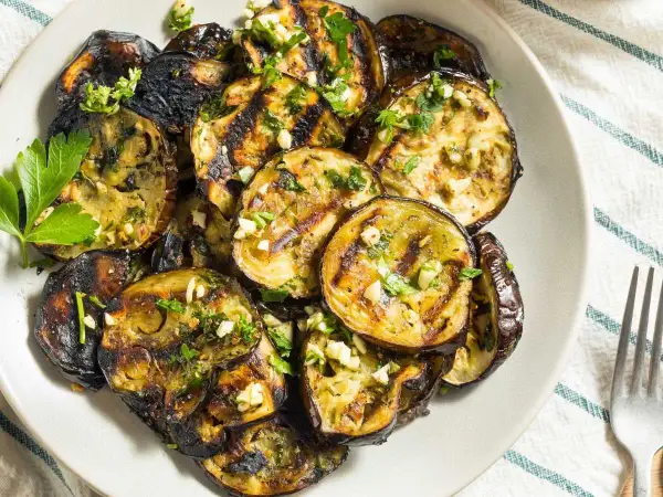 Rodajas de berenjena a la plancha, doradas y tiernas, con ajo picado y perejil fresco. Un plato delicioso y saludable.