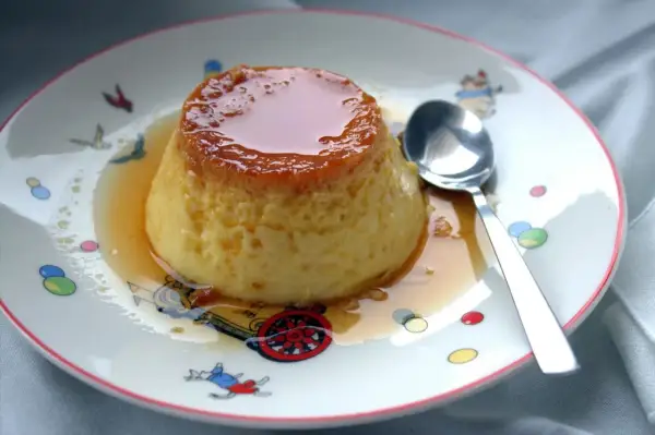 Delicioso flan de huevo casero, la receta de la abuela que nunca falla. Servido en un plato con dibujos infantiles y una cuchara lista para disfrutar.