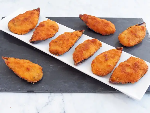 Mejillones tigre receta: mejillones rebozados y fritos, dorados y crujientes, servidos en una bandeja blanca sobre una pizarra.