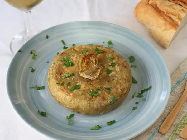 Tortilla de patatas con alcachofas de bote, decorada con perejil. Ideal para tus recetas con alcachofas de bote.