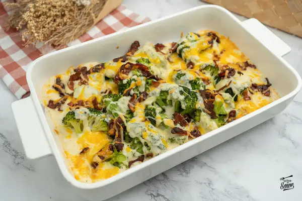 Delicioso brocoli al horno gratinado con queso y tocino crujiente, servido en una fuente blanca.