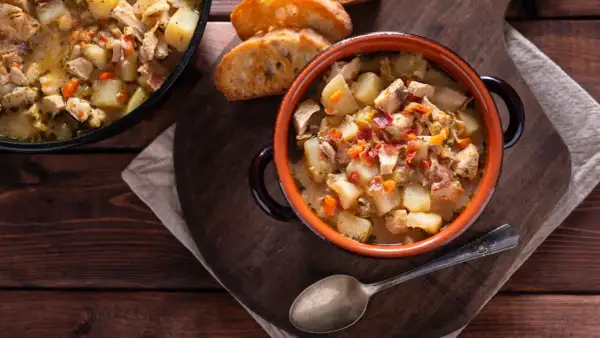 Un reconfortante guiso de pollo con patatas de la abuela, servido en cazuela de barro con pan tostado.