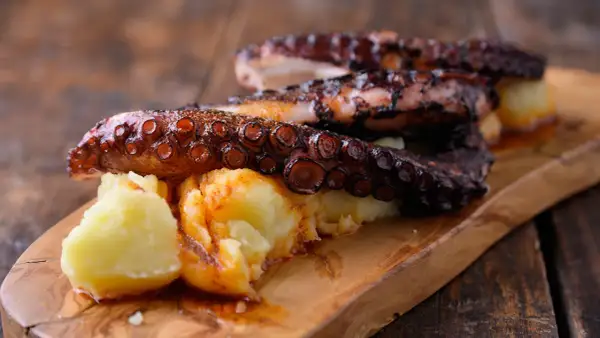Pulpo tierno con patatas y pimentón, servido en tabla de madera.