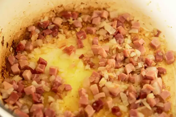 Guisantes con jamón, la receta de la abuela en plena cocción. Cebolla y taquitos de jamón dorándose en la sartén.