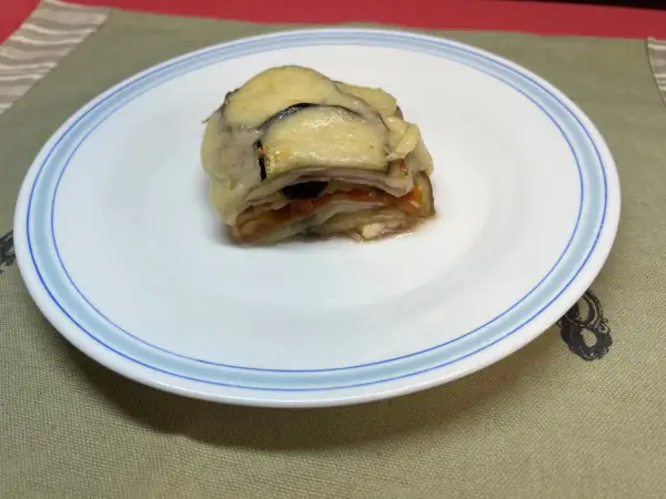 Un delicioso pastel de berenjenas gratinado con queso, servido en un plato blanco con borde azul.