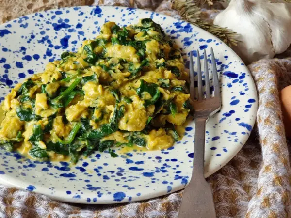 Un delicioso revuelto de espinacas cremoso, servido en un plato con salpicaduras azules. Un tenedor plateado descansa a un lado, listo para disfrutar.