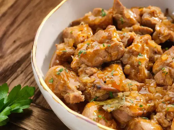 Un delicioso plato de caldereta de cordero, con trozos tiernos de carne en una salsa dorada y aromática, adornado con perejil fresco.