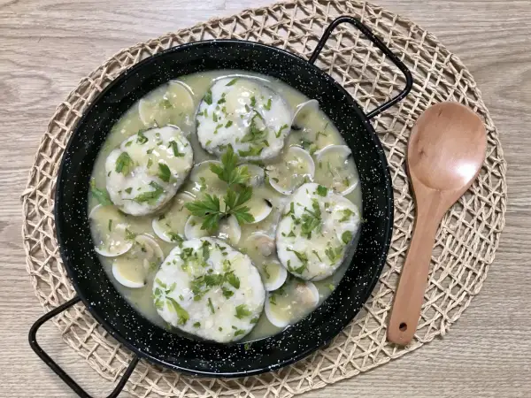 Merluza a la vasca, un plato tradicional con trozos de pescado blanco en una salsa cremosa con almejas y perejil picado.