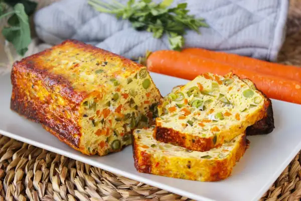 Pastel de verduras casero, con trozos visibles de zanahoria y guisantes, servido en una bandeja blanca.
