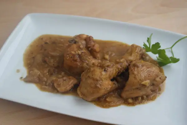 Sabroso pollo con almendras en una salsa dorada, servido en un plato blanco con una ramita de perejil.