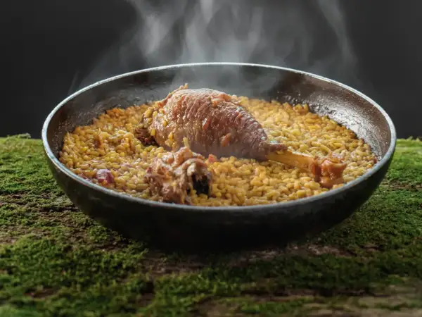 Arroz meloso con pitu de caleya, humeante y servido en paellera sobre un lecho de musgo.