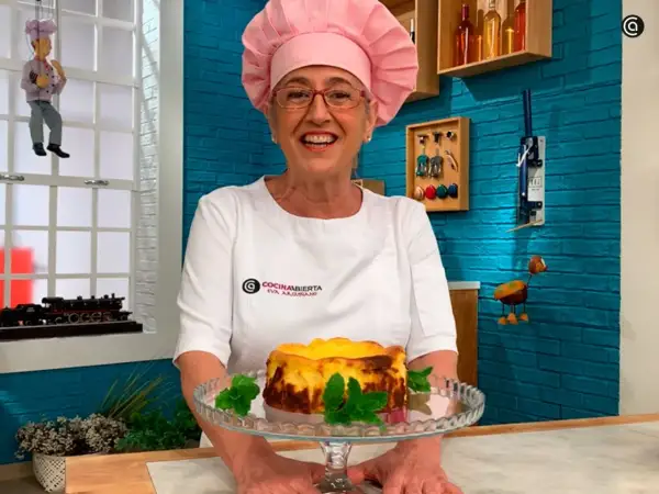 Eva Arguiñano sonríe con su delantal blanco y un gorro rosa, presentando una deliciosa tarta de queso.