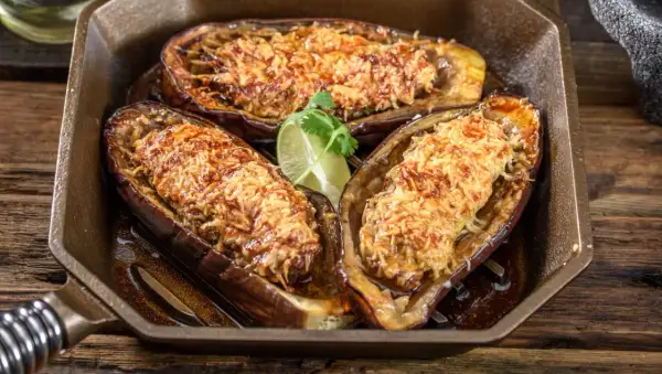 Berenjenas rellenas airfryer doradas y gratinadas, servidas en una sartén de hierro fundido con una rodaja de lima.