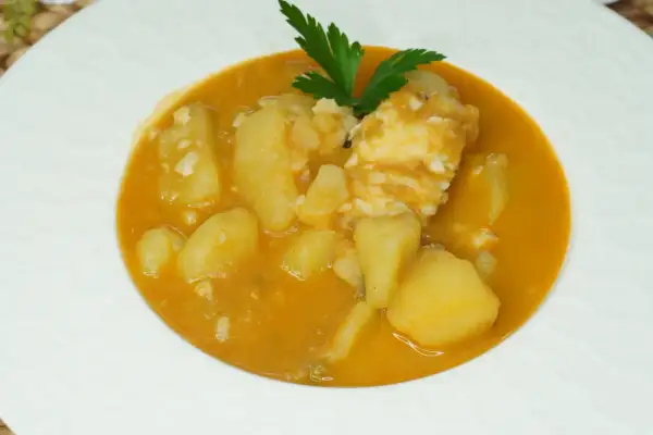 Un plato de patatas con bacalao en una salsa naranja, decorado con perejil.