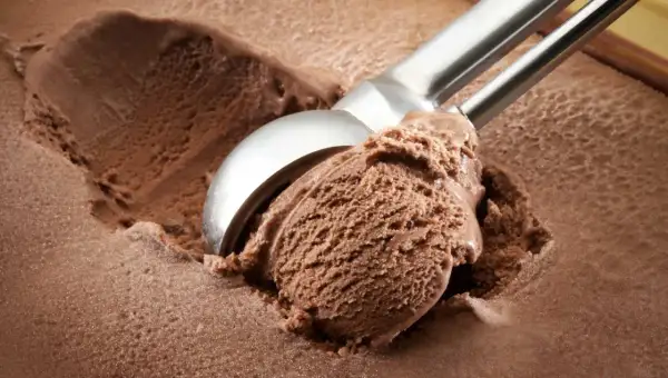 Cuchara saca una porción generosa de helado de chocolate casero, con textura cremosa y color intenso.