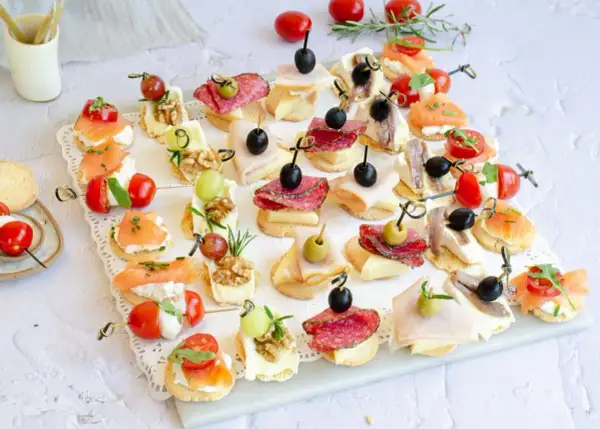 Variedad de canapés fríos fáciles y baratos: salmón, salami, jamón, queso, aceitunas, tomates cherry y más, perfectos para cualquier ocasión.