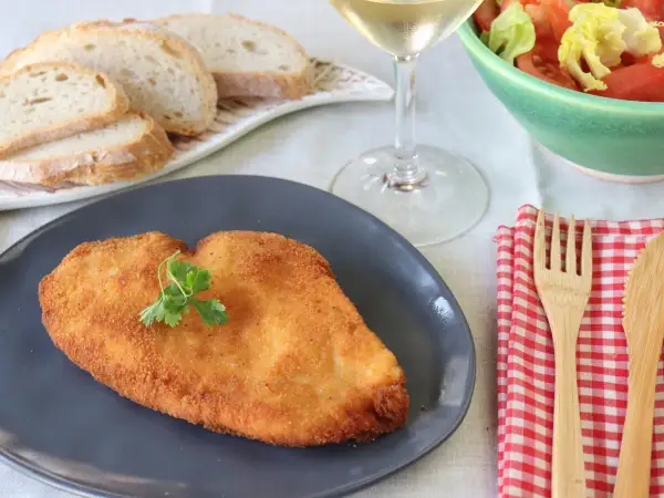 Un delicioso escalope de pollo dorado, servido con pan, ensalada y vino blanco.