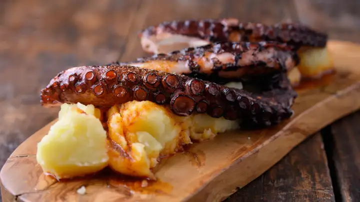 Pulpo tierno con patatas y pimentón, servido en tabla de madera.