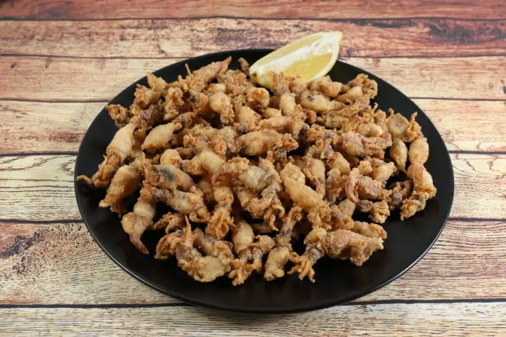 Un plato negro rebosante de puntillas de calamar crujientes, con un gajo de limón esperando para dar el toque final.